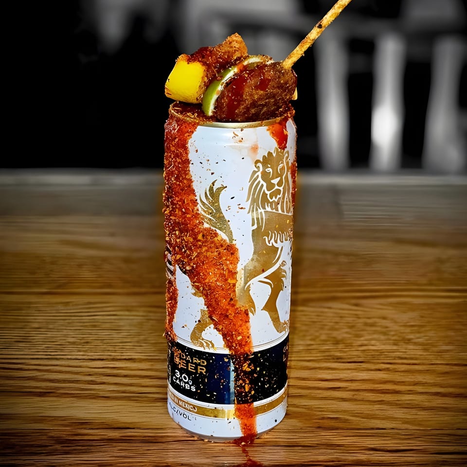 JD's Grill House michelada with a spiced rim, lime, and mango skewer on a wooden table.