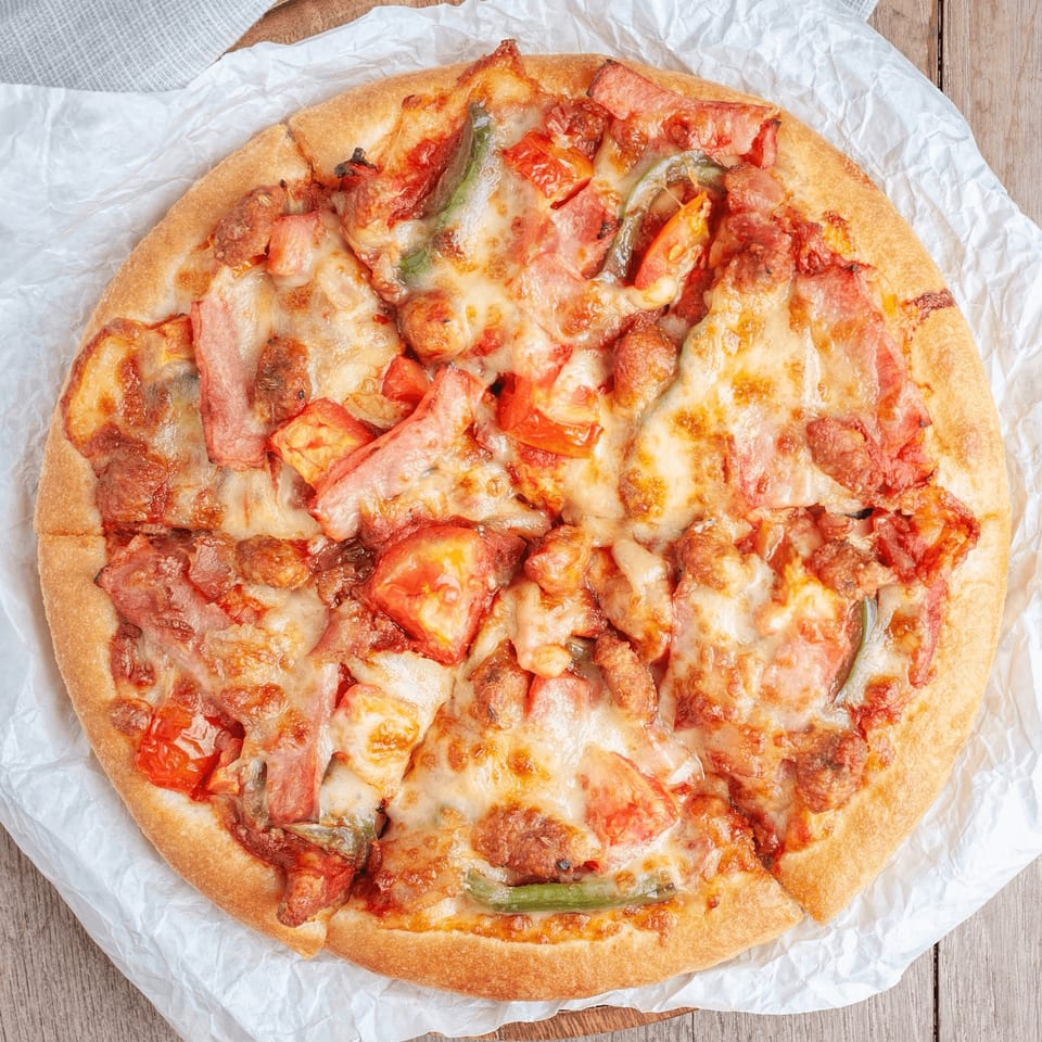 A JD's Grill House pizza with melted cheese, bacon, tomatoes, and green peppers on parchment paper.